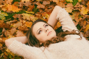 Woman laying in fall leaves looking up at the sky