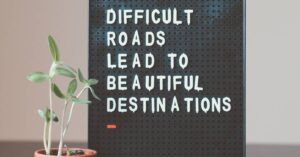 Plant next to a sign that says "Difficult roads lead to beautiful destinations"