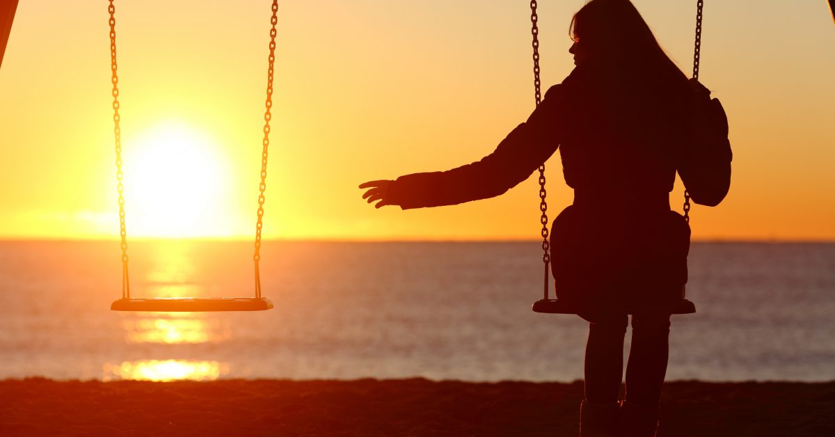 Woman on a swing at sunset reaching to an empty swing beside her